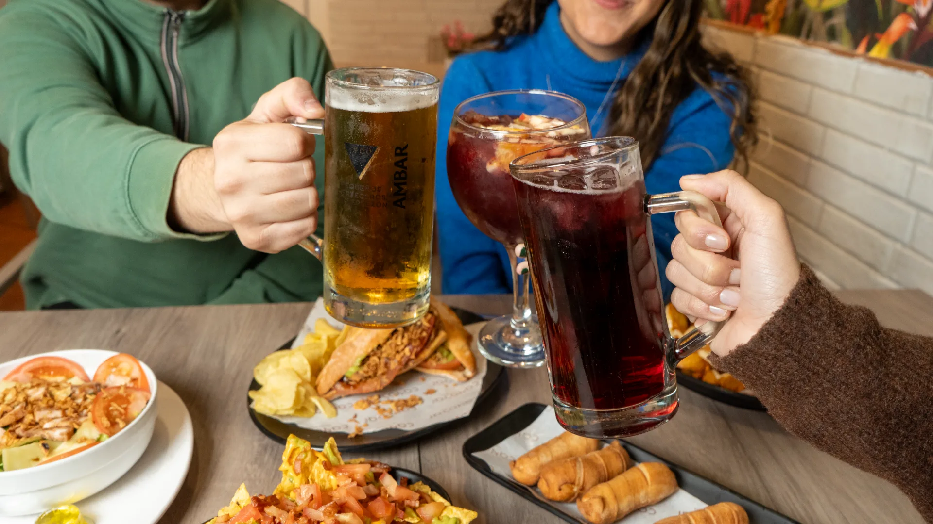 Brindis con cerveza y copas sobre una mesa llena de tapas