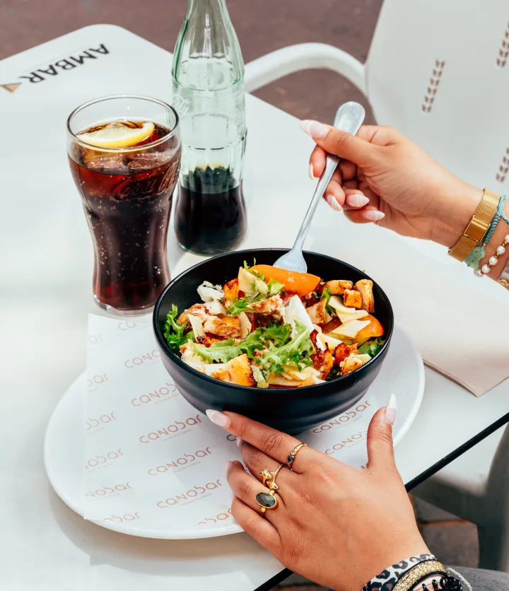 Ensalada en bol negro junto a un refresco, en la terraza