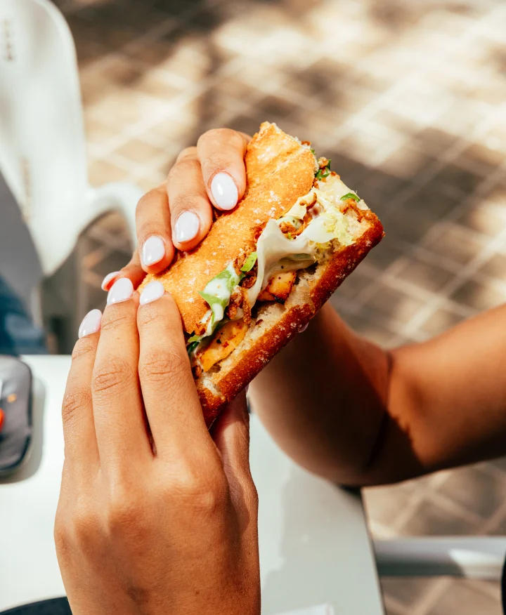 Primer plano de un bocata sujeto con las dos manos, con pan tostado y relleno abundante