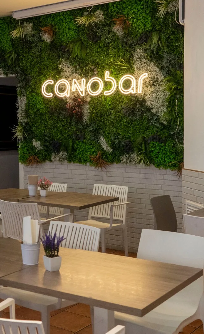 Interior de CanoBar: mesas de madera junto a la pared verde con el neón del bar